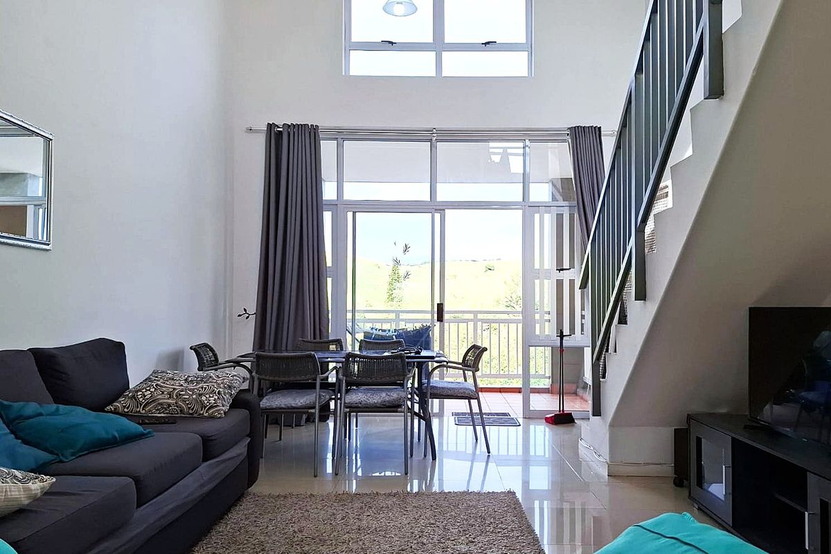 Spacious open-plan living area featuring double-volume ceilings, large sliding doors leading to a balcony, and a staircase with a modern metal balustrade.