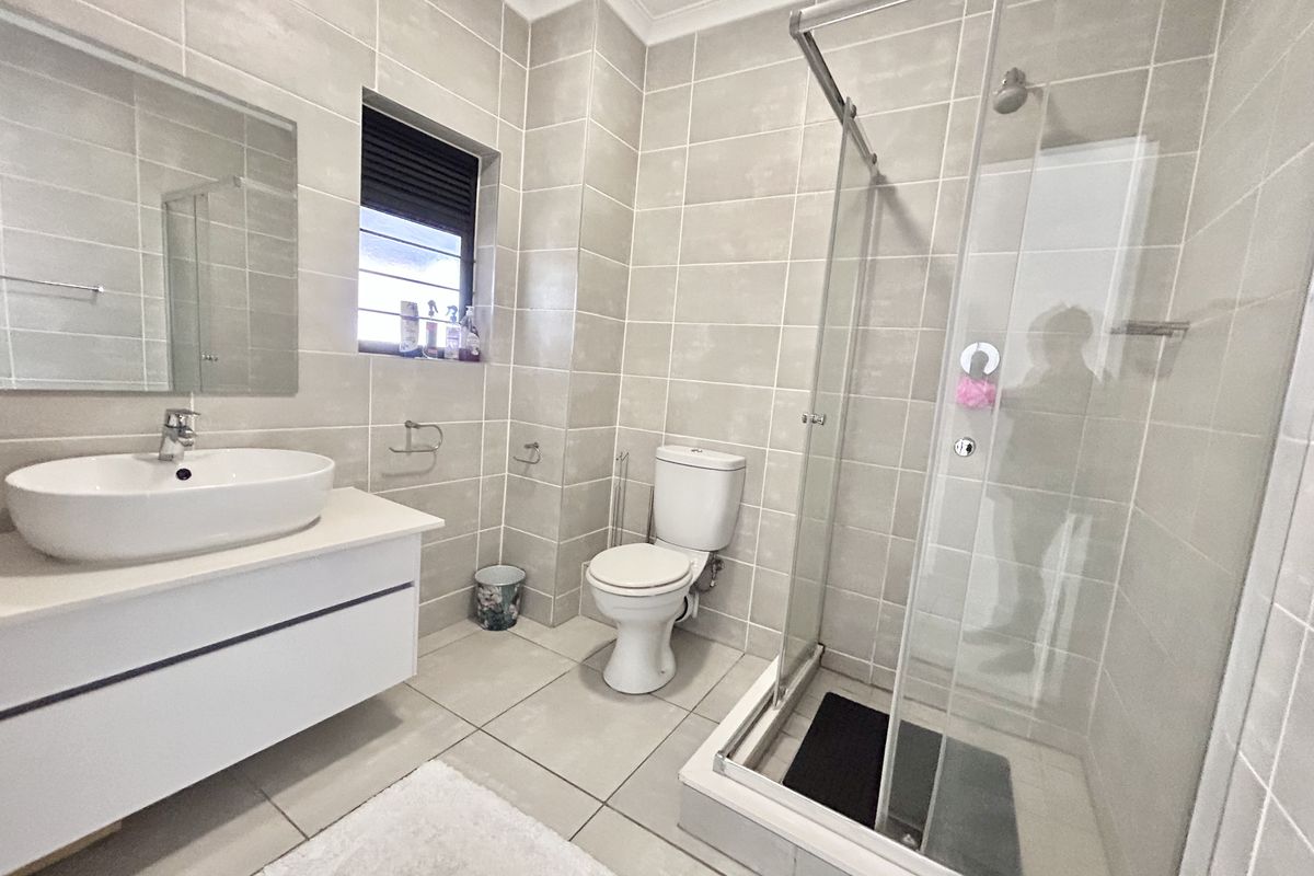 Modern bathroom featuring a vessel sink vanity, glass-enclosed shower, and neutral floor-to-ceiling tiling, providing a clean and functional space.