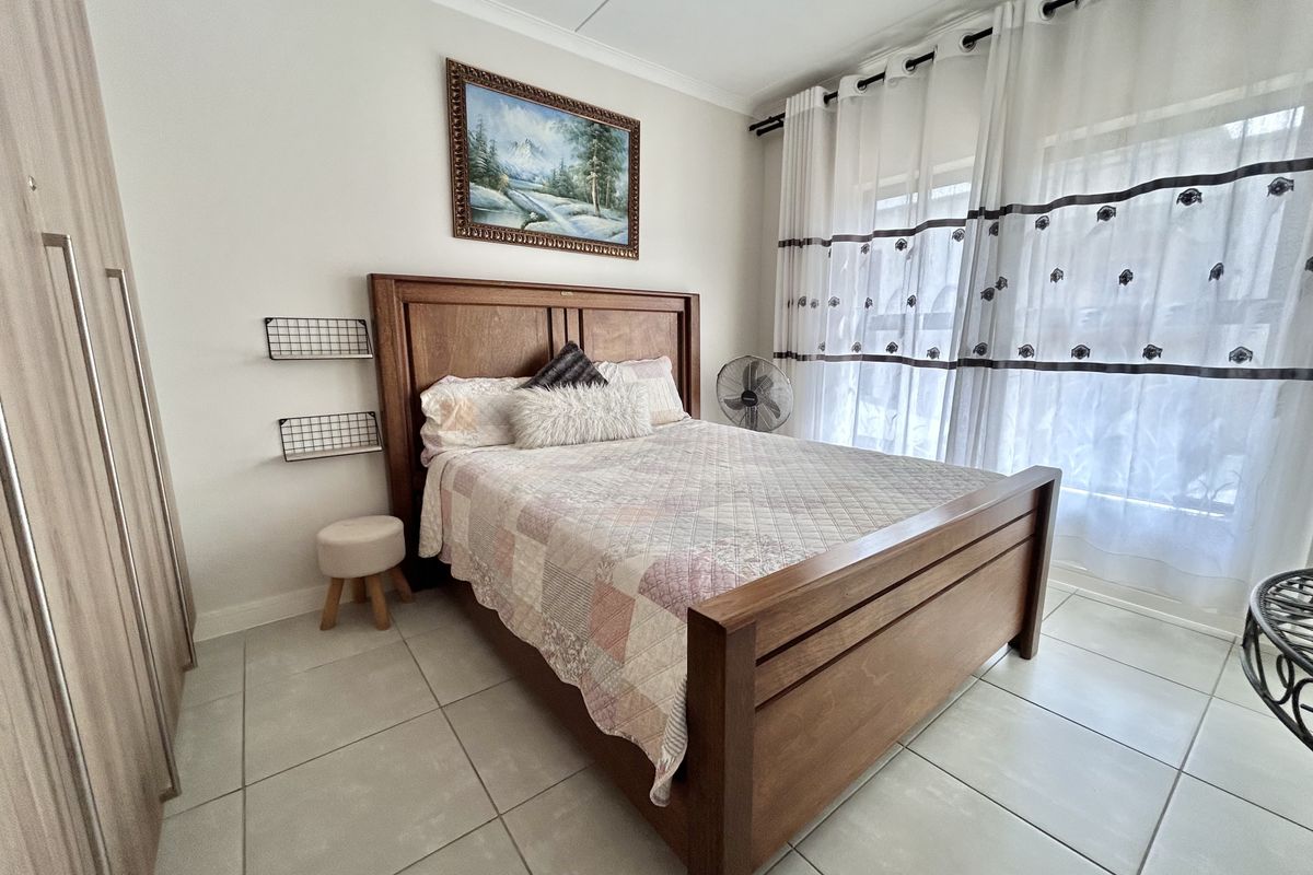 A well-maintained bedroom featuring neutral tiled flooring, a built-in wardrobe, and a ceiling fan, offering a clean and functional living space.