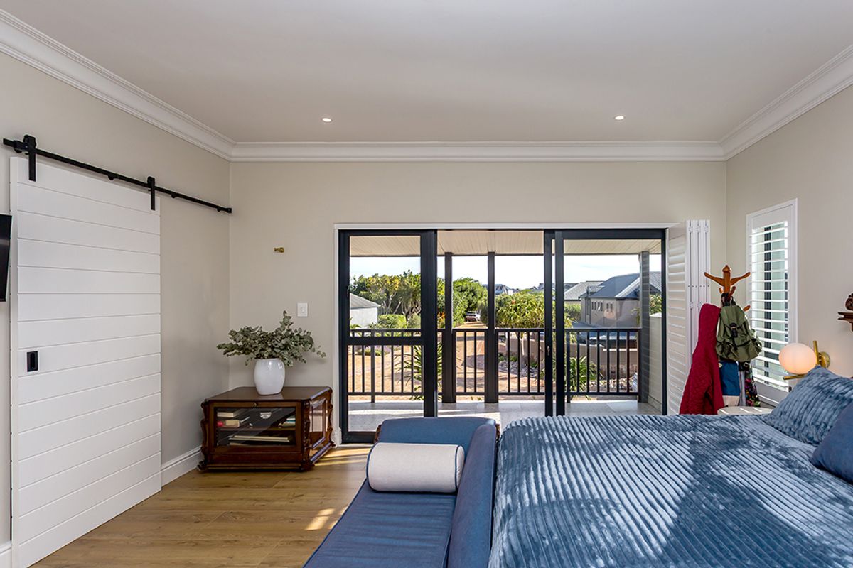 Spacious bedroom featuring modern wood-look flooring, crown molding, a sliding barn door, and large glass sliding doors opening onto a private balcony.