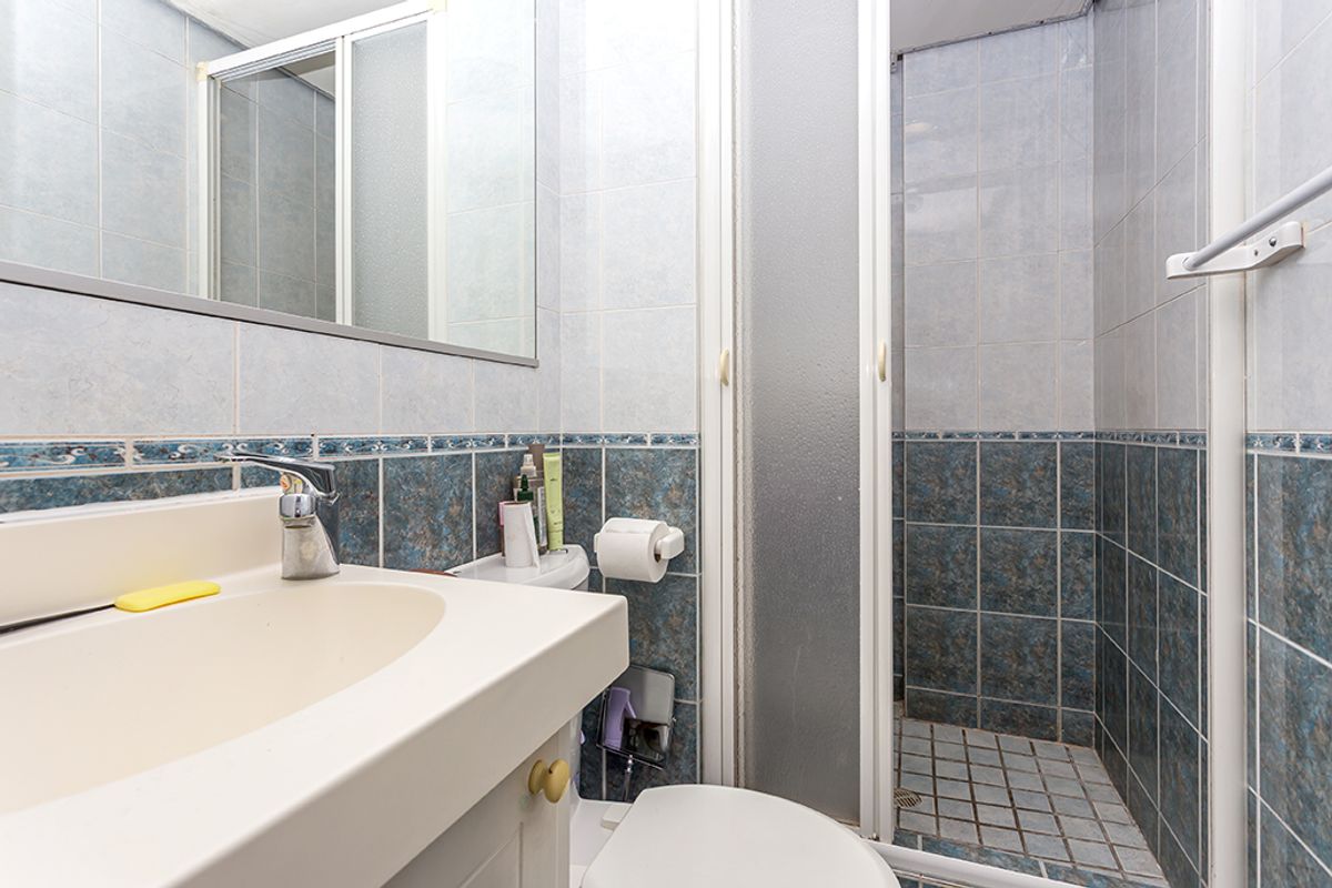 A compact bathroom featuring a vanity sink, a shower enclosure with sliding doors, and dated blue and white wall tiling.