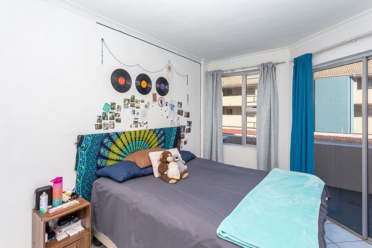 A bedroom featuring tiled flooring, a large window, and a sliding glass door providing access to an outdoor balcony area.