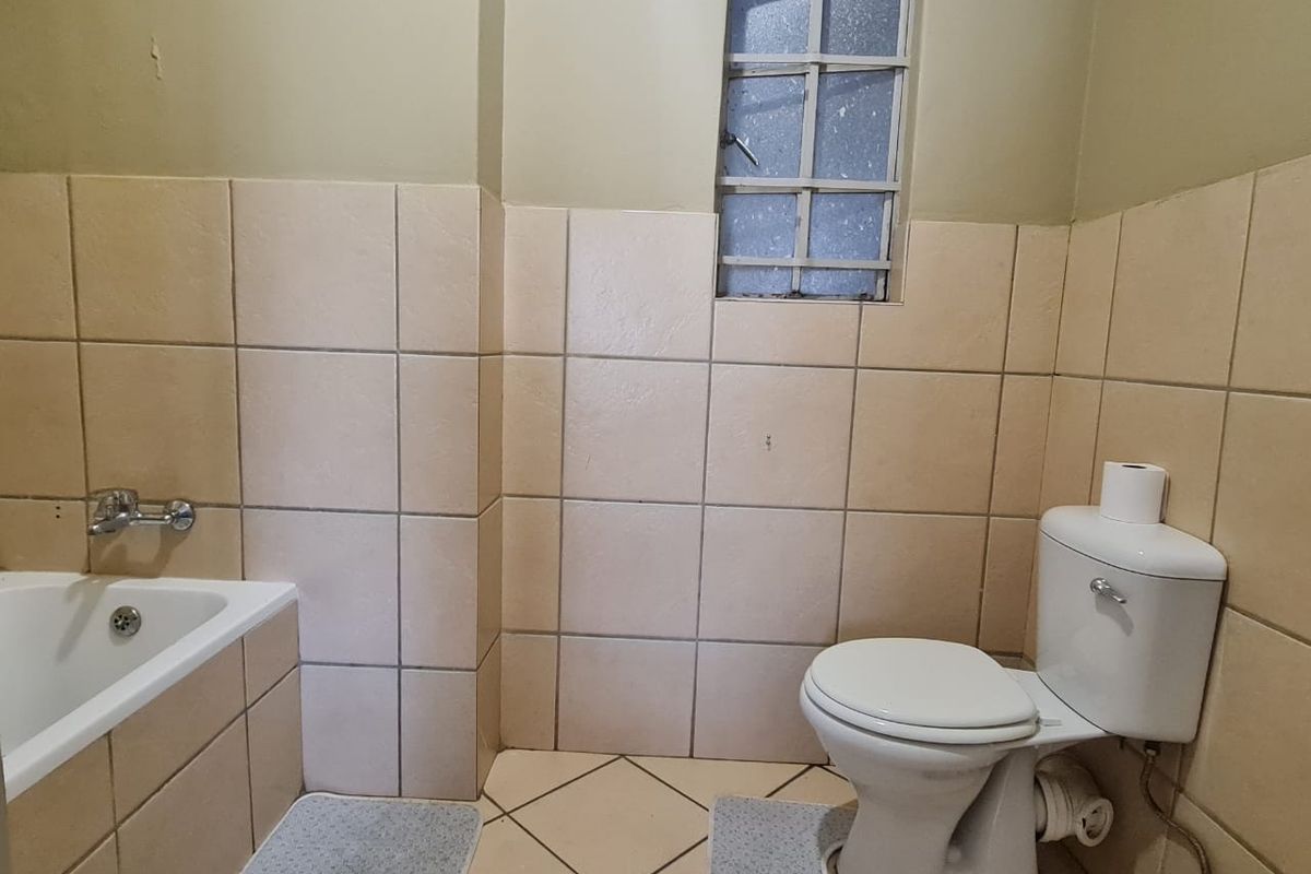 A dated bathroom featuring a standard bathtub, toilet, and tiled walls with a small high-set window.