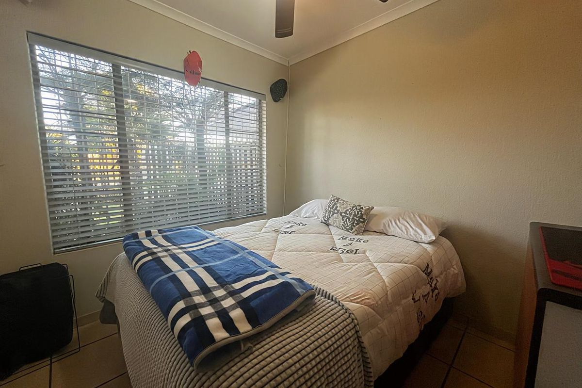 A functional bedroom featuring tiled flooring, a ceiling fan, and large windows with venetian blinds, offering a neutral space ready for personalization.