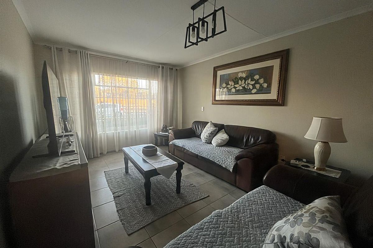A comfortable living room featuring tiled flooring, a modern pendant light fixture, and a large window allowing for natural light.