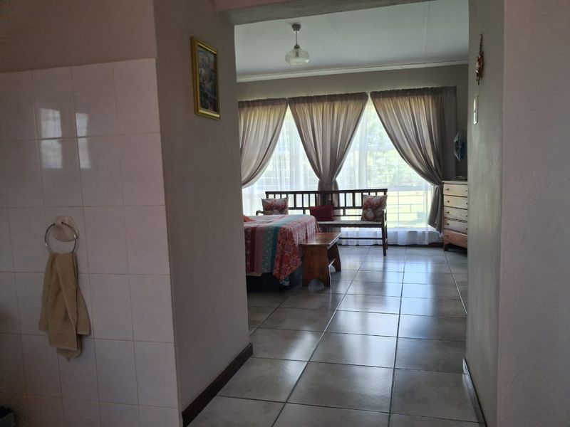 A bedroom featuring tiled flooring and a large window with curtains, viewed from an adjacent tiled hallway area.