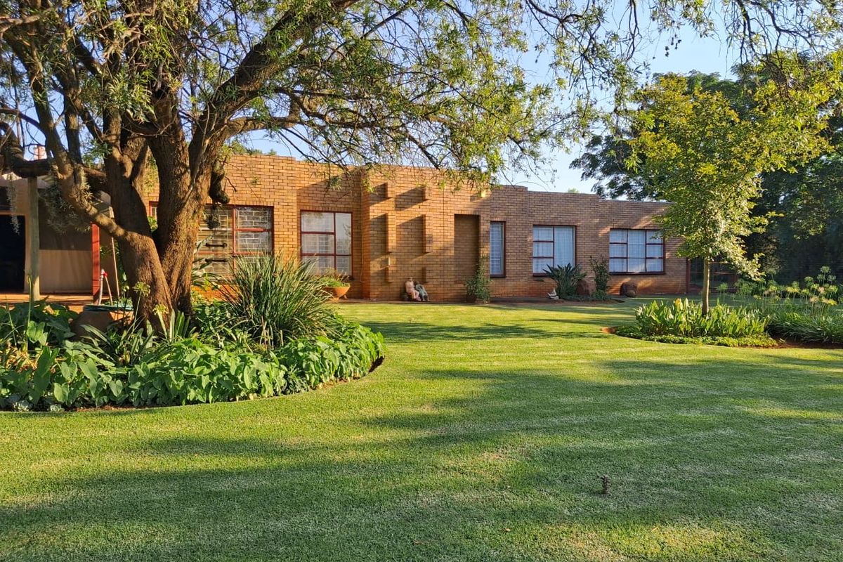 A well-maintained face brick farmhouse exterior featuring large windows, surrounded by a lush, manicured garden and mature trees.