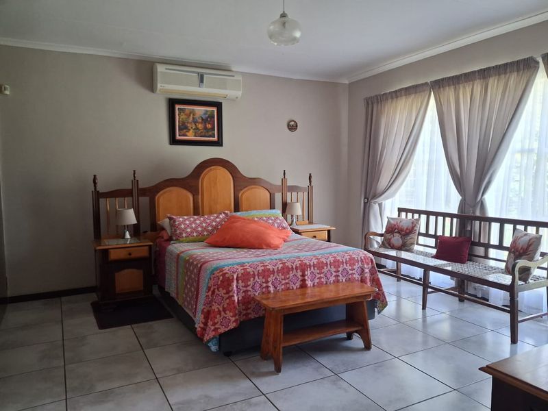 A spacious bedroom featuring tiled flooring, a wall-mounted air conditioning unit, and large windows with curtains allowing for natural light.
