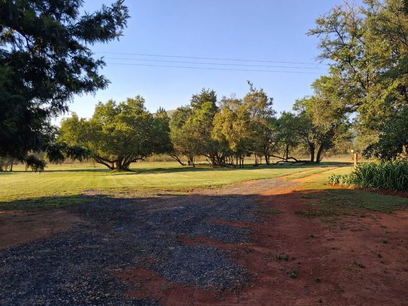 A spacious, well-maintained garden area featuring a gravel driveway leading through mature trees and expansive green lawns on the farm property.