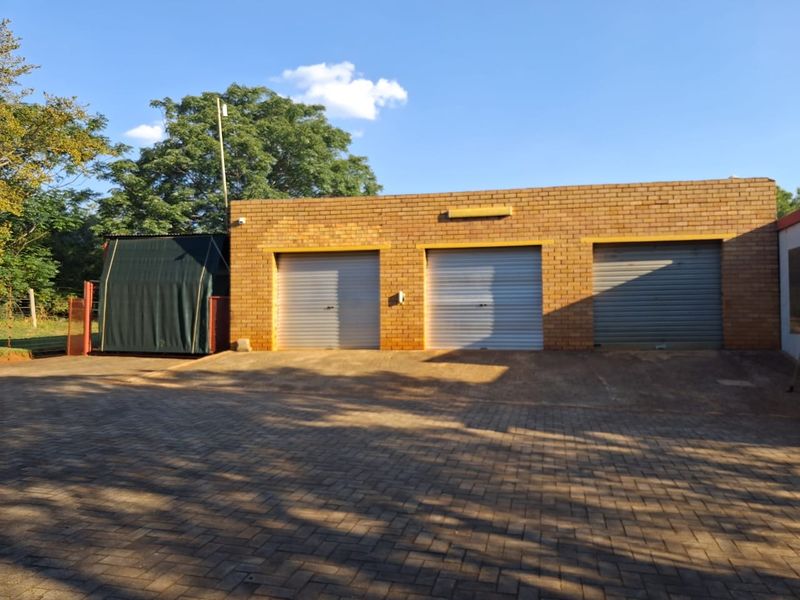A triple garage featuring face brick construction and secure roller shutter doors, set on a paved driveway within a farm property setting.