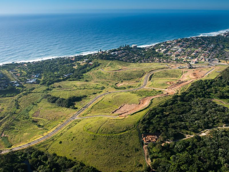 Aerial view of a coastal residential development site featuring established paved roads and expansive green terrain overlooking the ocean.