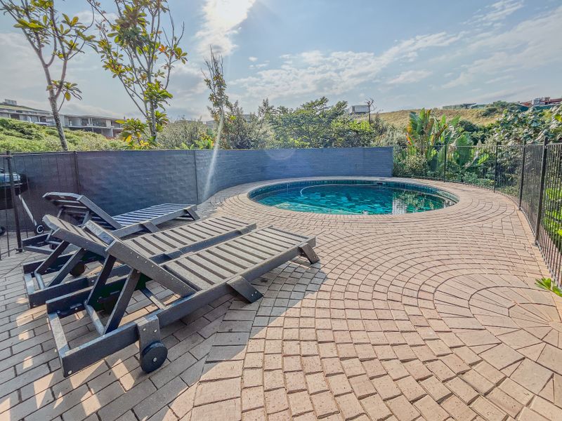A well-maintained circular swimming pool set within a paved deck area, featuring a retaining wall and secure perimeter fencing.