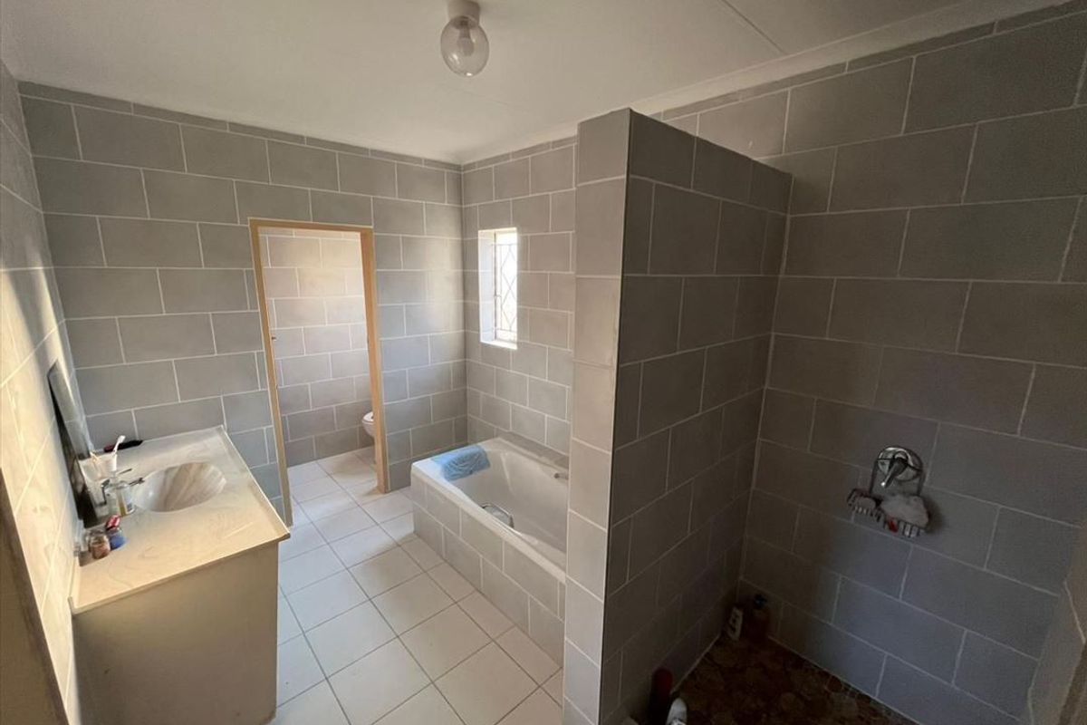 A functional bathroom featuring a built-in vanity, a drop-in bathtub, and a separate walk-in shower area with grey tiled walls.