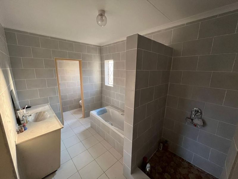A functional bathroom featuring a built-in vanity, a drop-in bathtub, and a separate walk-in shower area with grey tiled walls.
