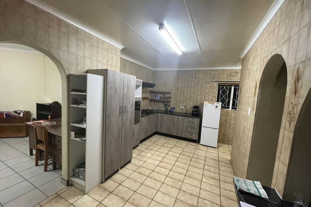 A functional kitchen featuring built-in cabinetry, laminate countertops, and ceramic tiling throughout, with an arched entryway leading to an adjacent living space.
