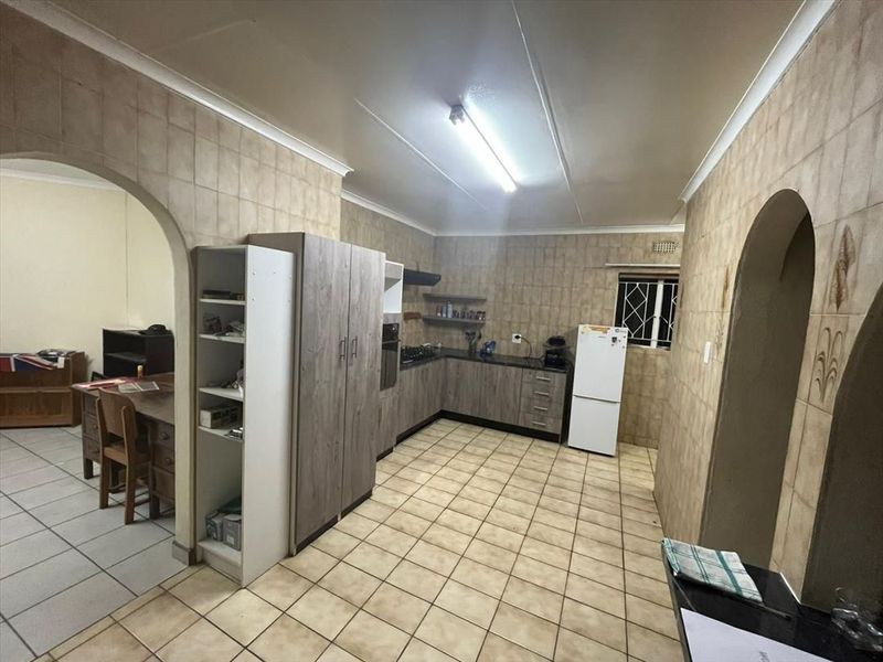 A functional kitchen featuring built-in cabinetry, laminate countertops, and ceramic tiling throughout, with an arched entryway leading to an adjacent living space.