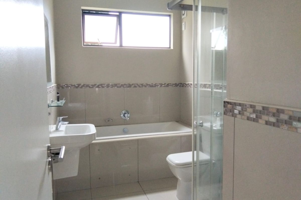 A modern bathroom featuring a built-in bathtub, wall-mounted basin, toilet, and a glass-enclosed shower with neutral tiled finishes.