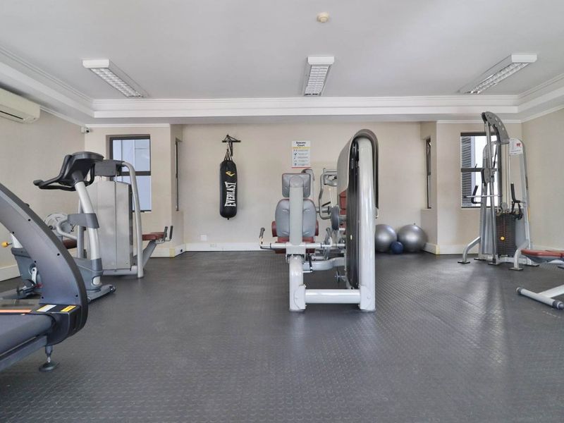 A well-maintained communal gym facility featuring rubberized flooring, wall-mounted air conditioning units, and various fixed exercise equipment.