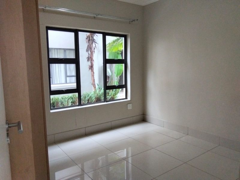 A bright, empty bedroom featuring neutral tiled flooring, large aluminum-framed windows, and a clean, minimalist aesthetic ready for personalization.