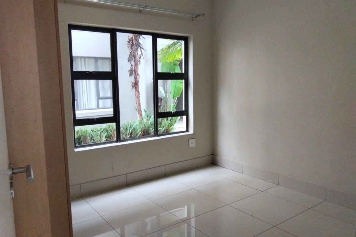 A bright, empty bedroom featuring neutral tiled flooring, large aluminum-framed windows, and a clean, minimalist aesthetic ready for personalization.