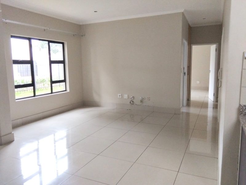 A bright and spacious open-plan living area featuring neutral tiled flooring, recessed downlighting, and large windows allowing for ample natural light.