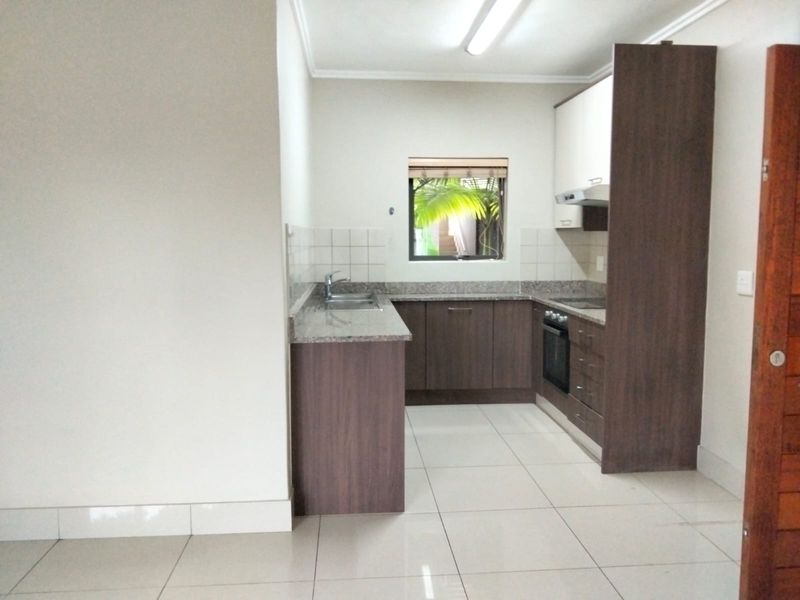 A clean, functional kitchen featuring dark wood cabinetry, granite countertops, a built-in oven, and tiled flooring.