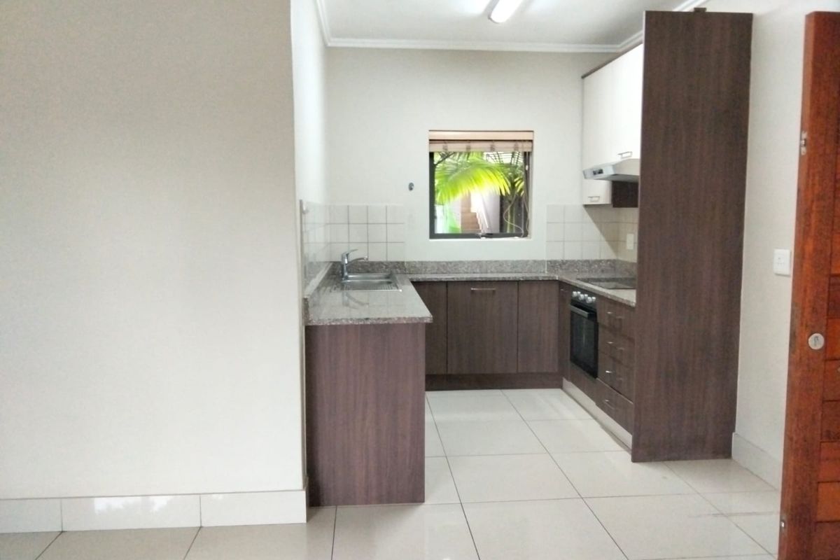 A clean, functional kitchen featuring dark wood cabinetry, granite countertops, a built-in oven, and tiled flooring.