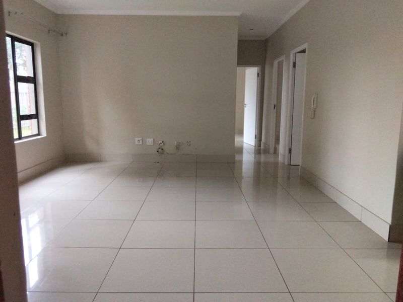 An empty living area featuring neutral tiled flooring, clean walls, and access to adjacent rooms, providing a versatile space for customization.