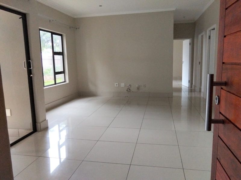 An empty, open-plan living area featuring polished porcelain floor tiles, neutral wall finishes, and a sliding glass door leading to an outdoor space.