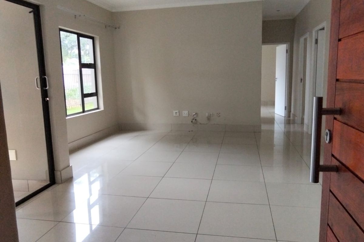 An empty, open-plan living area featuring polished porcelain floor tiles, neutral wall finishes, and a sliding glass door leading to an outdoor space.