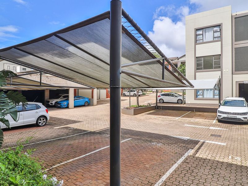 Exterior view of the apartment complex parking area featuring paved surfaces and covered shade-cloth parking bays.