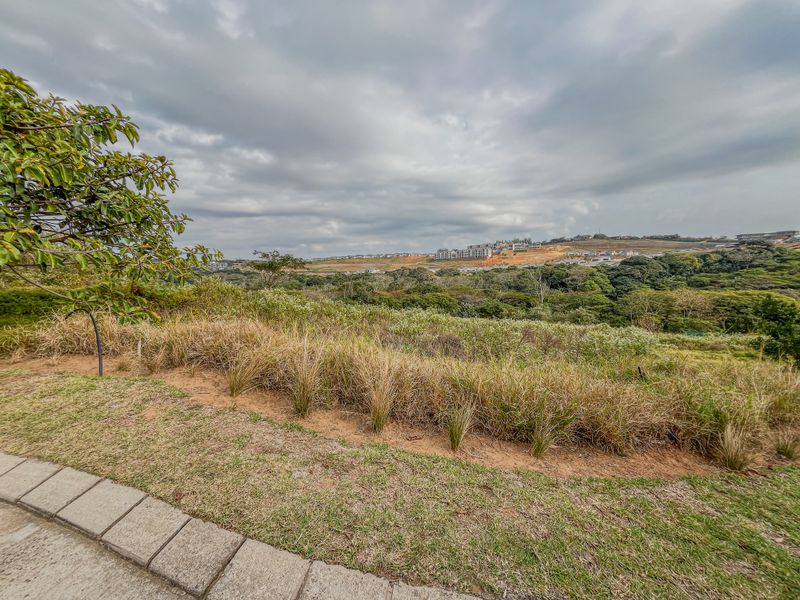 A scenic view overlooking a natural landscape and distant residential development from the edge of the vacant residential property.