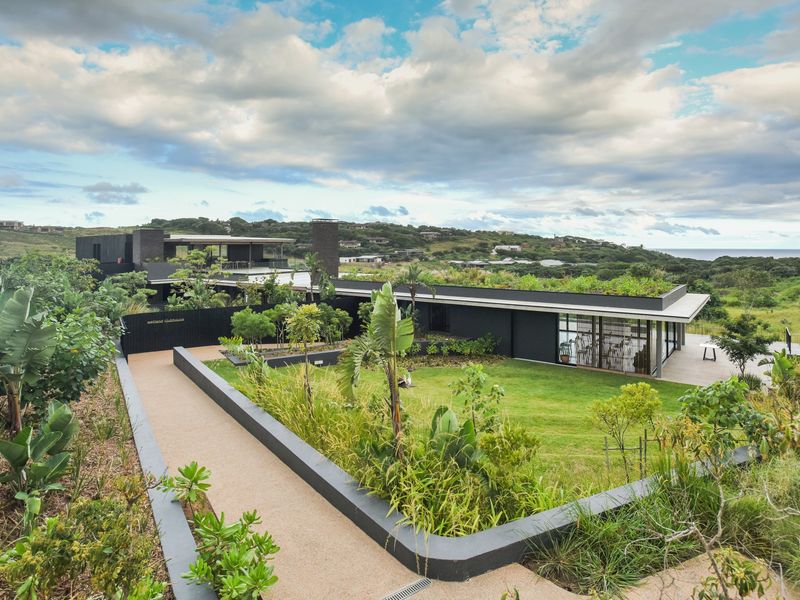Modern clubhouse facility featuring a green roof, landscaped gardens, and expansive decking, set within a scenic coastal estate environment.