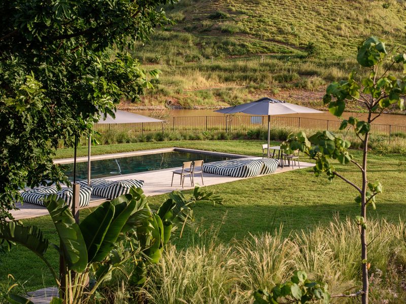 A well-maintained swimming pool area featuring timber decking, surrounded by landscaped lawns and overlooking a scenic water feature and hillside.