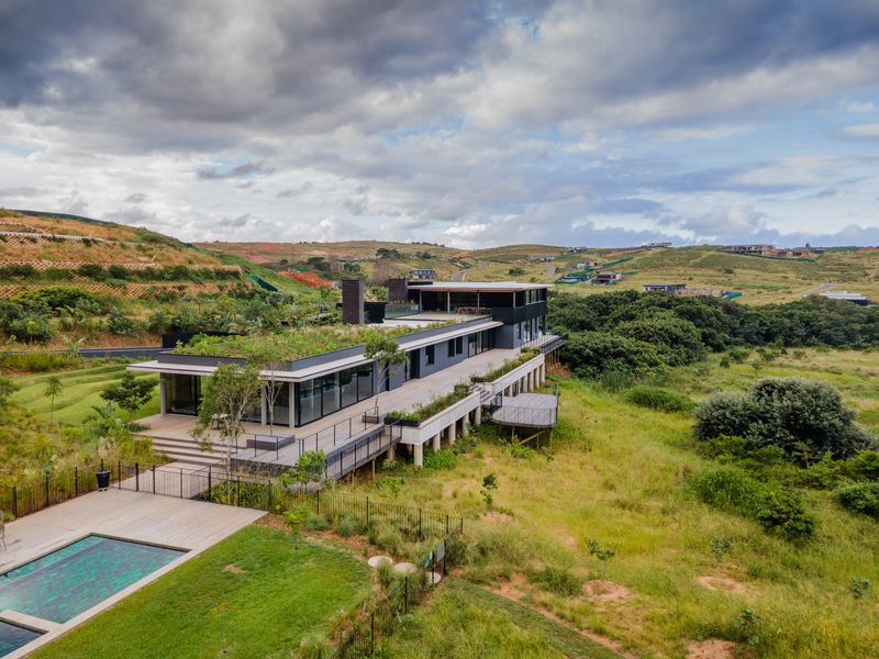 Aerial view of a modern architectural residence featuring a green roof, expansive timber decking, and a private swimming pool set in a landscaped estate.