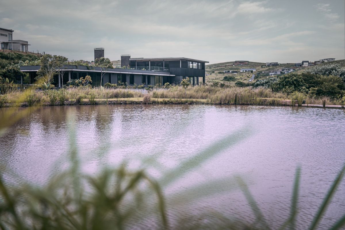 A modern architectural residence overlooking a serene pond and landscaped grounds, showcasing contemporary design and seamless integration with the natural environment.