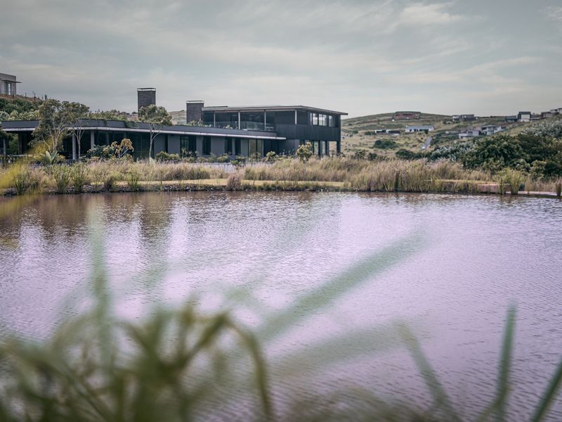 A modern architectural residence overlooking a serene pond and landscaped grounds, showcasing contemporary design and seamless integration with the natural environment.