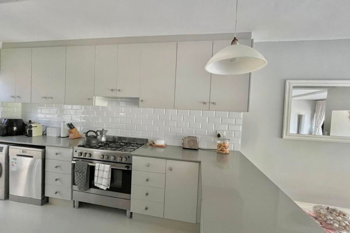 Modern kitchen featuring light grey cabinetry, stone countertops, subway tile backsplash, and a stainless steel gas stove with extractor fan.