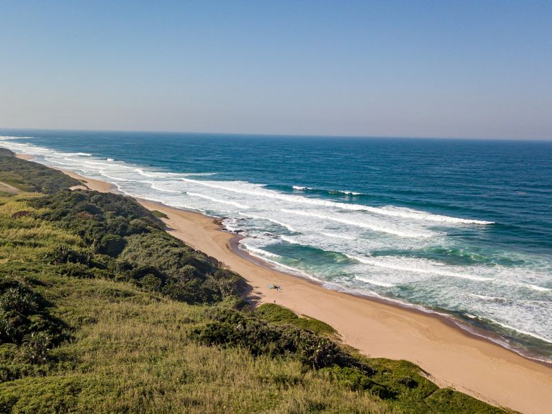 An aerial view of the pristine coastline, showcasing the expansive sandy beach and natural coastal vegetation adjacent to the vacant land.