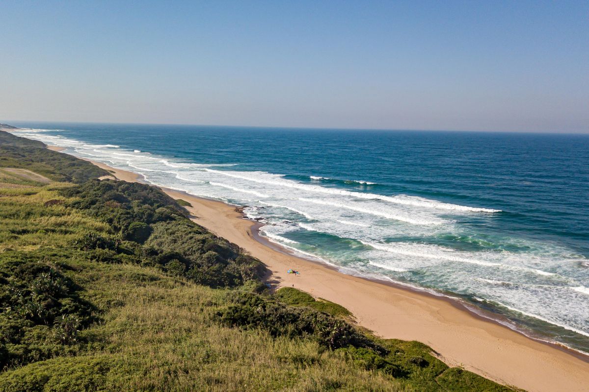 An aerial view of the pristine coastline, showcasing the expansive sandy beach and natural coastal vegetation adjacent to the vacant land.
