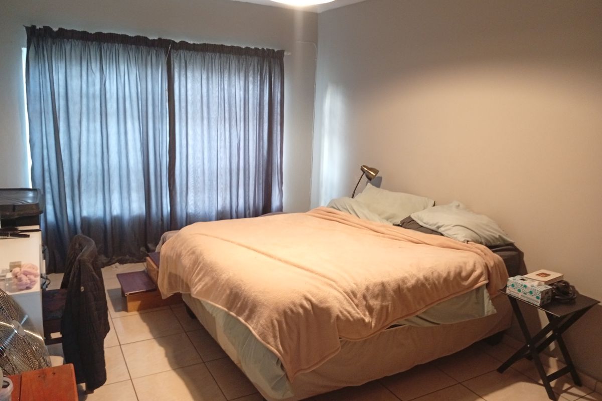 A functional bedroom featuring tiled flooring and large window treatments, providing a neutral space ready for personalization.