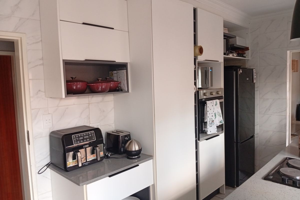 Modern kitchen featuring white cabinetry, stone countertops, built-in oven, and marble-look wall tiling.