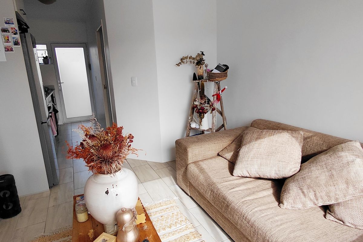 A living room area featuring tiled flooring and access to an adjacent hallway and kitchen space.