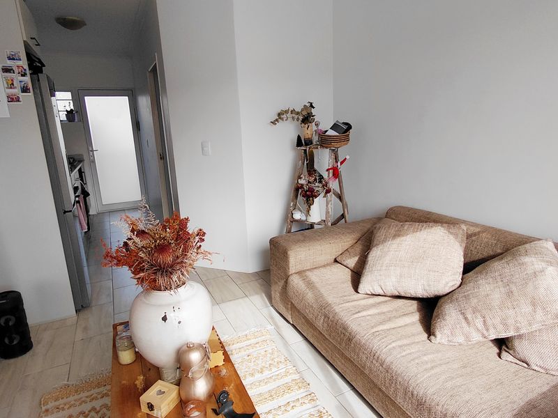 A living room area featuring tiled flooring and access to an adjacent hallway and kitchen space.