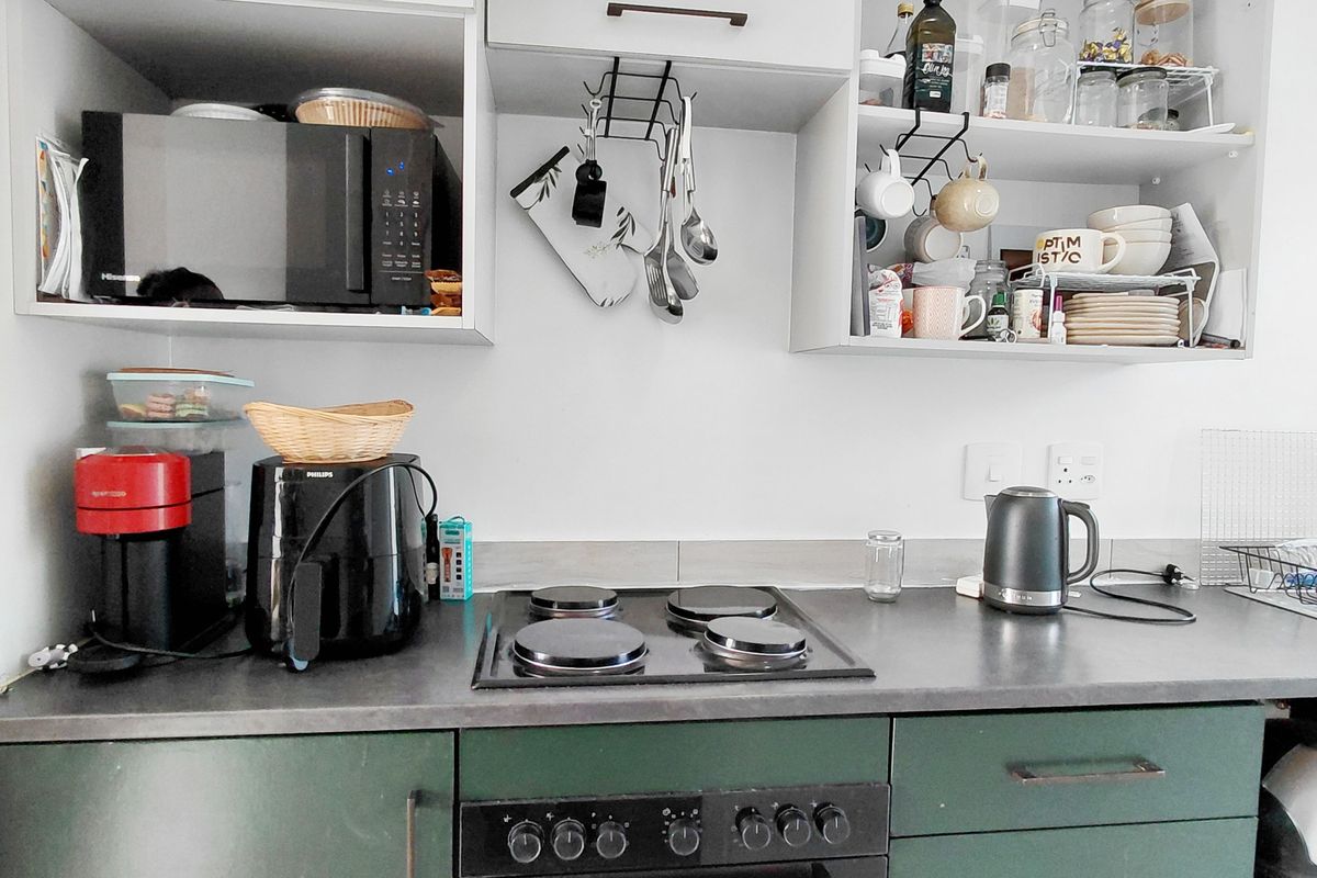 A compact kitchen area featuring dark green lower cabinetry, a built-in electric oven and hob, and open upper shelving for storage.