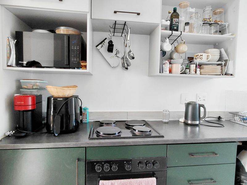 A compact kitchen area featuring dark green lower cabinetry, a built-in electric oven and hob, and open upper shelving for storage.