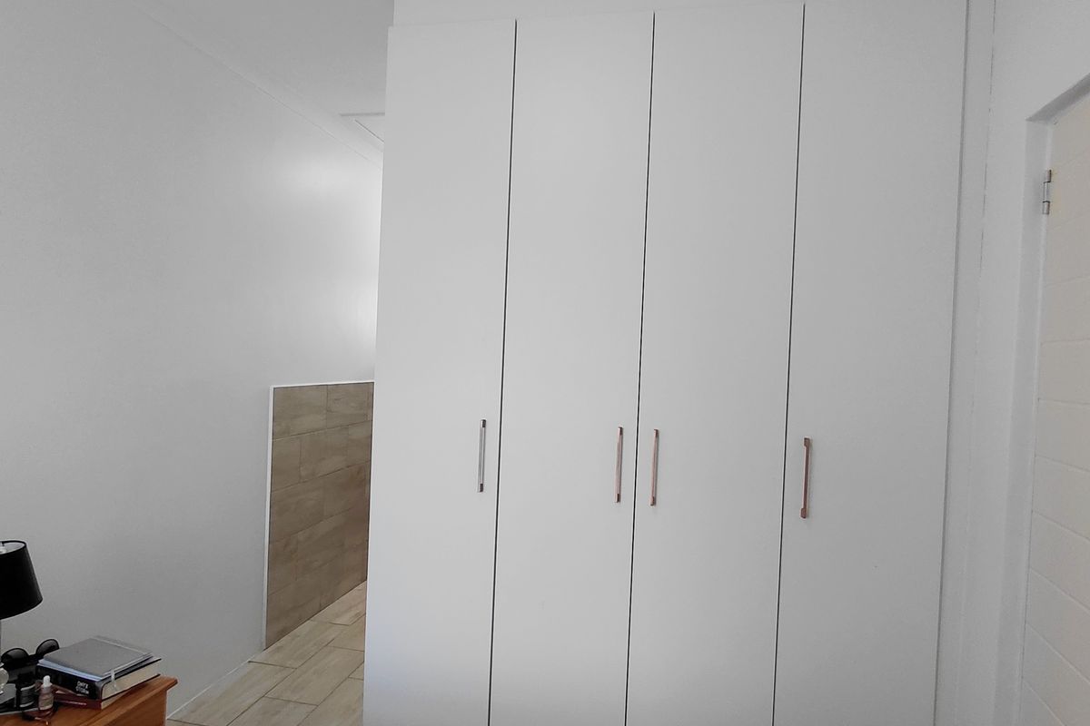 A bedroom featuring modern white built-in cupboards and light-toned tiled flooring, providing clean lines and ample storage space.