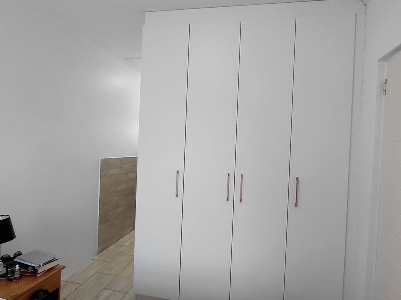 A bedroom featuring modern white built-in cupboards and light-toned tiled flooring, providing clean lines and ample storage space.