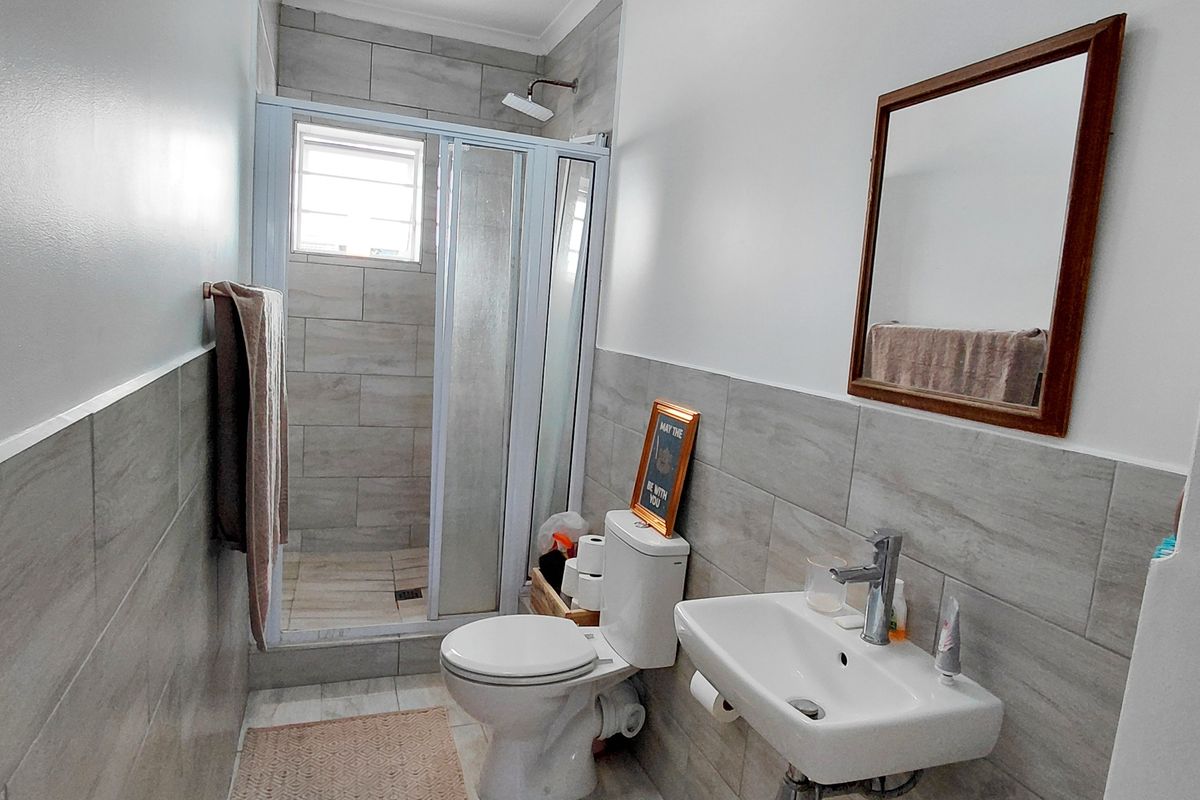 A modern bathroom featuring a tiled shower enclosure, wall-mounted basin with mixer tap, and a standard toilet with neutral grey wall and floor tiling.