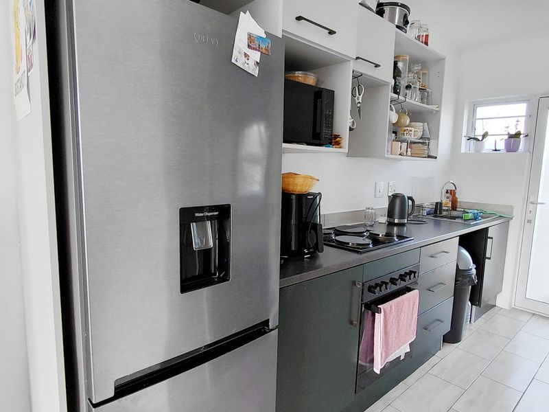 A functional kitchen featuring dark cabinetry, laminate countertops, built-in oven, hob, and tiled flooring with direct access to an exterior door.